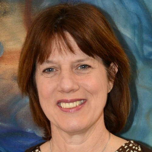 Smiling woman with brown hair in front of a colorful abstract background.