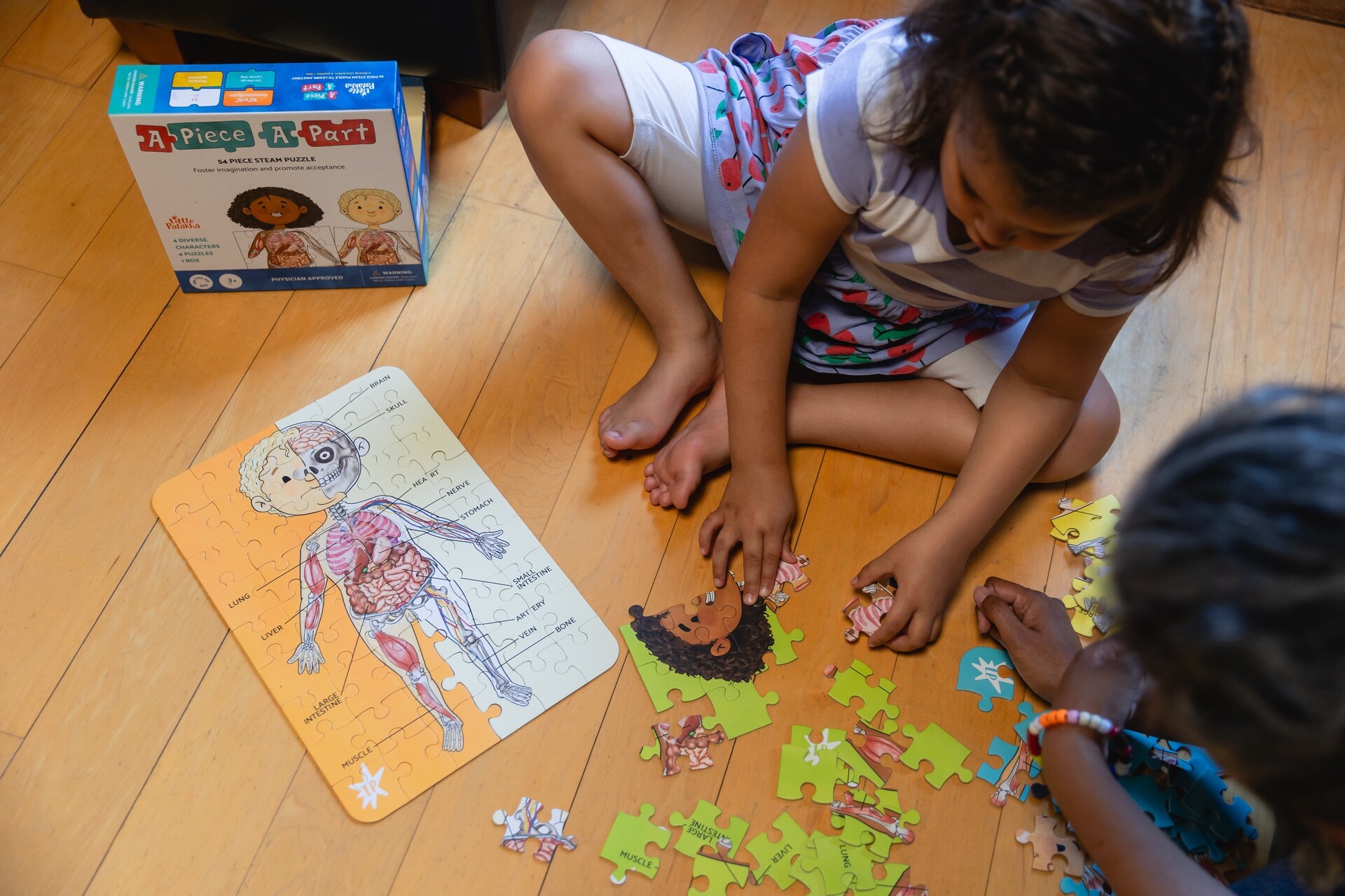 Two children are assembling a body anatomy puzzle on the floor.