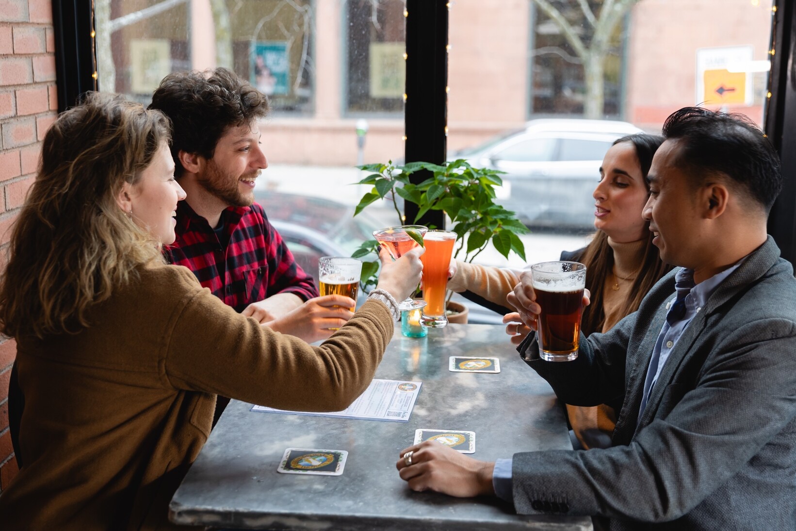 Four friends enjoy drinks at a bar, smiling and laughing together.