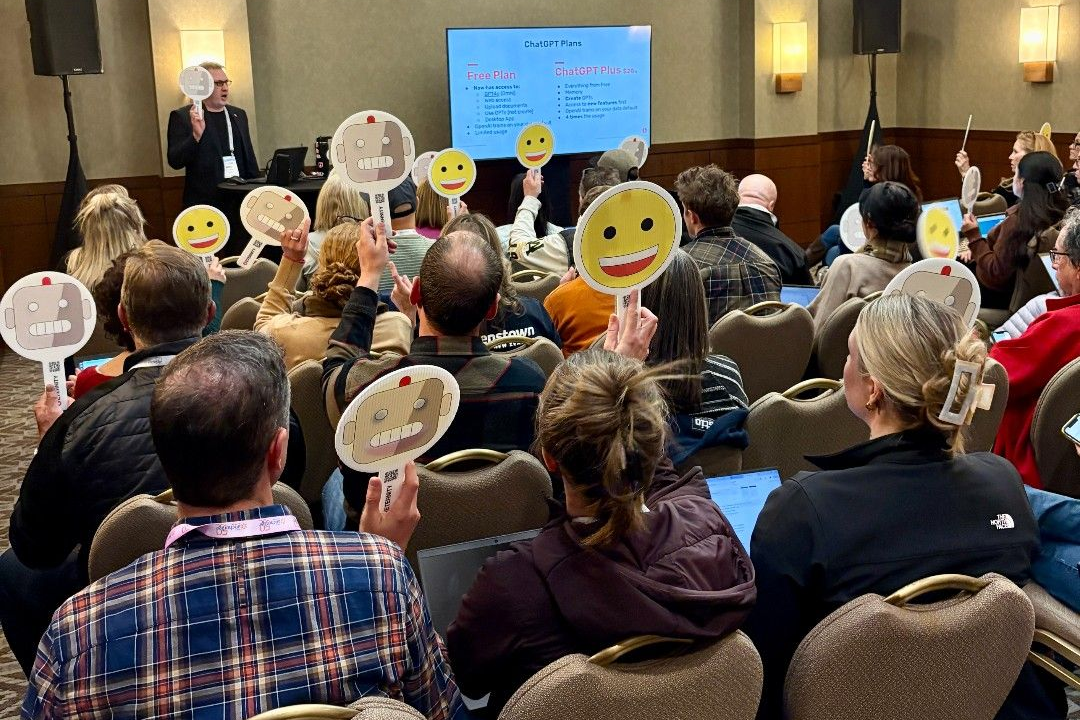 Audience members raise emoji signs during a presentation on ChatGPT plans.