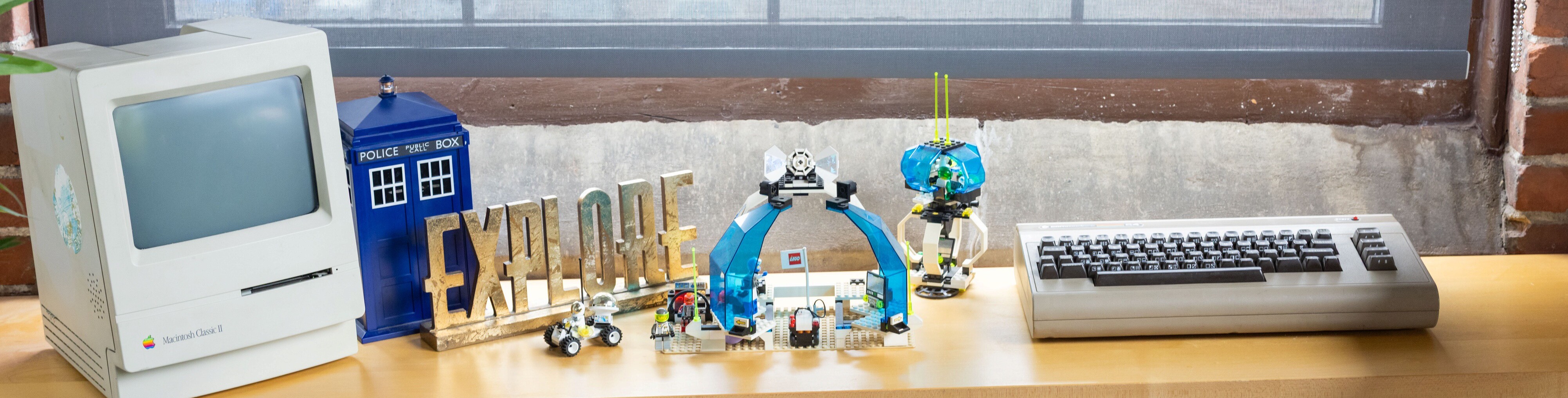 A vintage Macintosh computer, LEGO builds, and an "EXPLORE" sign on a wooden desk.