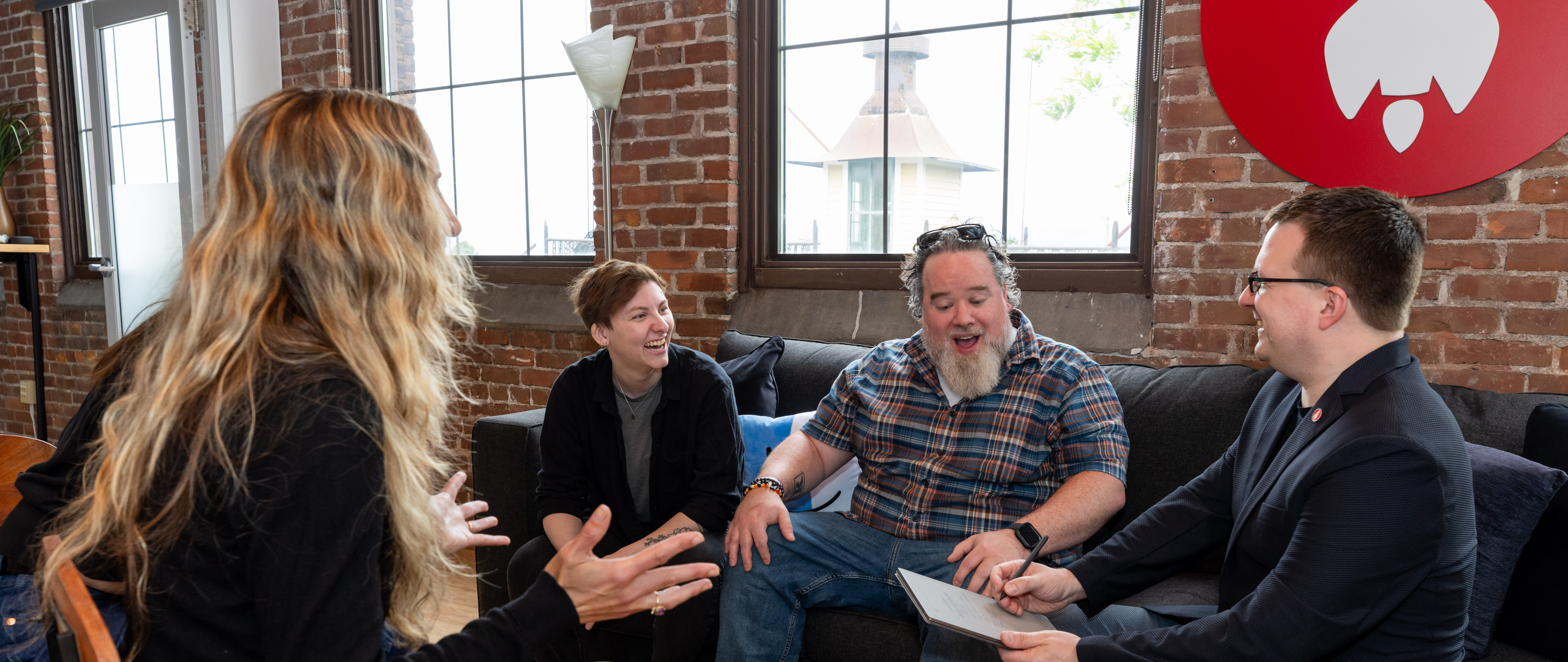 Four people engaged in lively discussion in a cozy, brick-walled setting.
