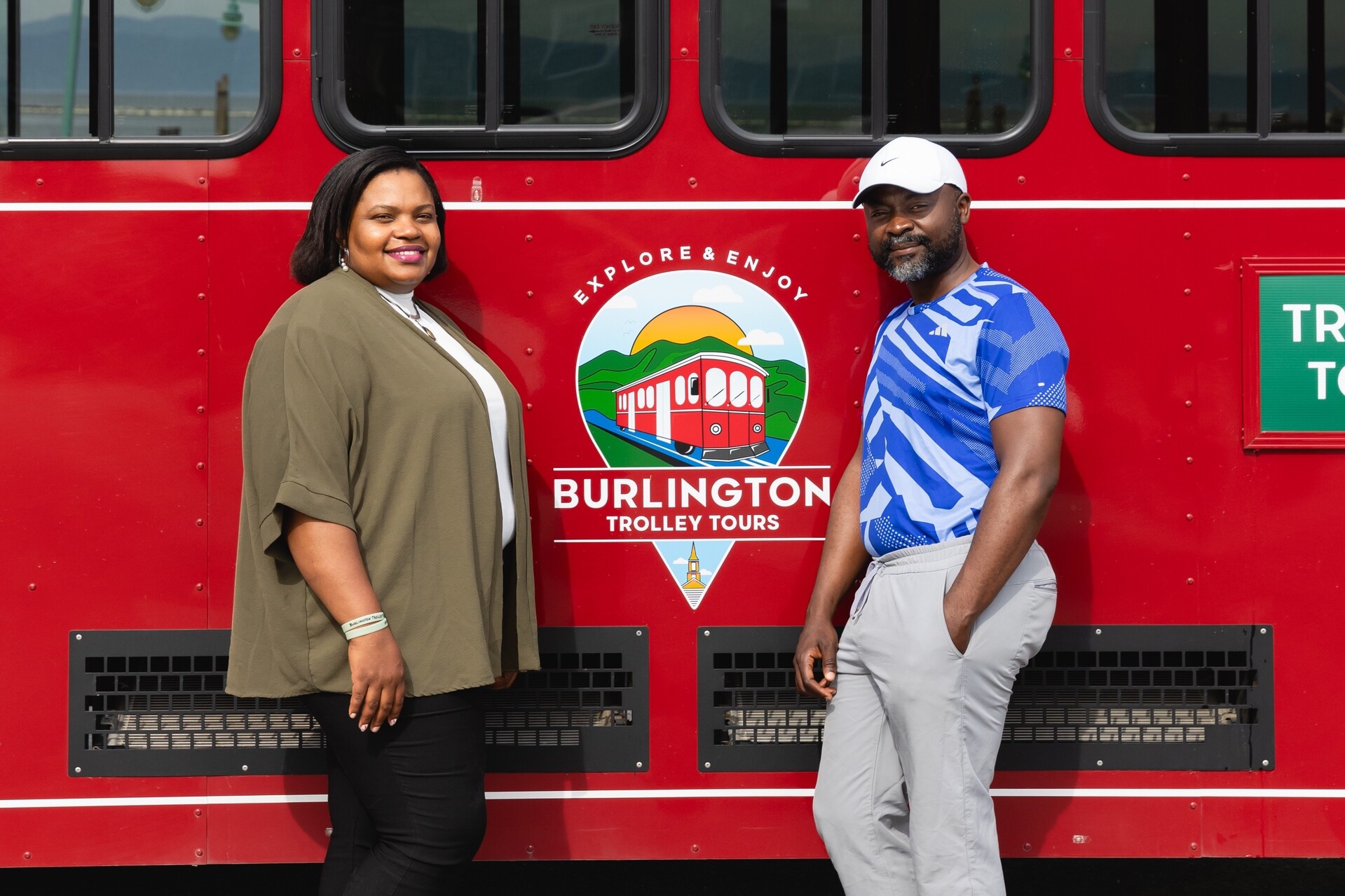 Two people pose next to a red trolley tour vehicle in Burlington.
